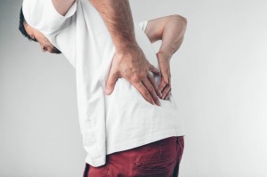 Long working hours and health. Young male with backache. Man with back pain on gray background.